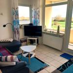 Wohnzimmer mit TV, Sitzgelegenheiten und Blick auf Balkon.