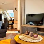 Wohnzimmer mit Fernseher, Couch und Esstisch im Hintergrund.