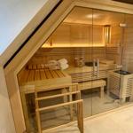Sauna mit Holzbank, Handtuch und Heizung. Glasfront und Dachschräge sichtbar.
