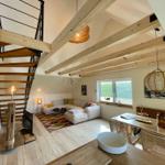 Wohnbereich mit Sofa, Tisch und Fenster. Holzdecken und Treppe sichtbar.