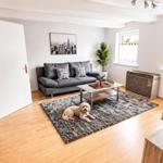Wohnzimmer mit grauem Sofa, Glas-Tisch und Fellteppich. Ein Hund liegt darauf.