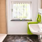 Badezimmer mit Dusche, Waschbecken und Fenster mit grünen Handtüchern.