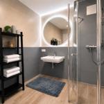 Badezimmer mit Dusche, Waschbecken und Regal. Holzfußboden und graue Fliesen.