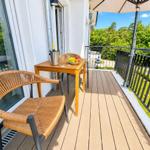 Terrasse mit Tisch, Stühlen und Sonnenschutz. Blick auf grüne Bäume und einen gepflegten Garten.