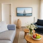Wohnzimmer mit Sofa, Sessel, Tisch und Fernseher an der Wand.