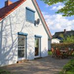 Wohnhaus mit Terrasse, Garten und Tisch mit Stühlen. Dach mit roten Ziegeln und blauen Fensterrahmen.