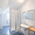 Badezimmer mit Dusche, Waschbecken und Spiegelschrank. Fliesenboden und Dachschrägen.