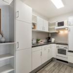 Küche mit weißen Schränken, Herd, Kühlschrank und Mikrowelle.