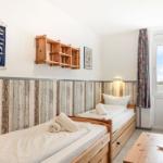 Zwei Einzelbetten mit Holzgestell, Fenster mit Blick auf Wasser, Wanddekoration und Holzregal.