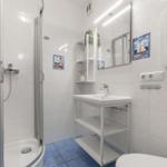 Badezimmer mit Dusche, Waschbecken und Toilette. Weiße Fliesen und blaue Bodenfliesen.