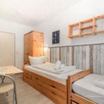 Zimmer mit zwei Betten, Schreibtisch, Kleiderschrank und Wandregal.