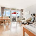 Wohnung mit Schlafzimmer, Wohn- und Essbereich sowie Balkon mit rotem Sonnenschirm.