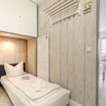 Schlafzimmer mit Bett, Kleiderhaken und Schrank. Durchgang zu Wohnbereich mit Fenster.