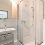 Badezimmer mit Dusche, Waschbecken und Spiegel.
