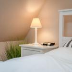 Bedroom with white bed, nightstand, and lamp. A plant hangs on the wall.