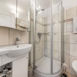 Bathroom with shower, sink, and toilet. Tiled wall and mirror cabinet.