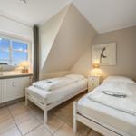 Two single beds in an attic room with window and nightstand.