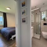 Schlafzimmer mit Bett und Fenster. Nebenraum mit Dusche, Toilette und Waschbecken.