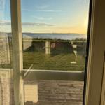 Blick auf einen See durch eine Glasschiebetür mit Holzterrasse und Rasenfläche.