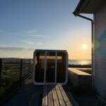 Außenliegende Sauna mit Blick auf Wasser und Sonnenuntergang neben Haus.