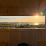 Sicht aus Holzsauna auf Sonnenuntergang über Wasser und Grünflächen