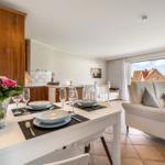 Dining table with placemats, chairs, and flowers. Living area with sofa and garden view.