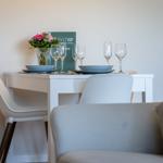 A white table with chairs, plates, and glasses. Flowers and a book are on it.