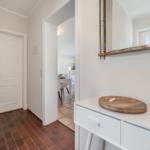 Hallway with white walls, brown floor, and mirror above cabinet