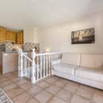 Living area with sofa, kitchen area, and staircase with white balustrade.
