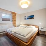 Bedroom with wooden bed, white nightstands, and wooden wardrobe. Window with floral curtains.