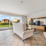 Living room with sofa, TV, and view of garden and houses.