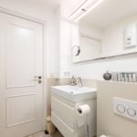 Badezimmer mit Waschbecken, Spiegel und Heizung. Toilette und Handtuchhalter sichtbar.