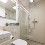 Badezimmer mit Dusche, Waschbecken und Toilette. Moderne Einrichtung mit Spiegel und Licht.
