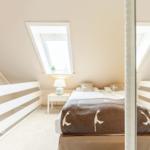 Dachgeschosszimmer mit Dachschrägen, Dachfenster und Bett mit Decke.