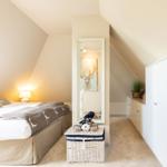Schlafzimmer mit Dachschrägen, Bett, Spiegel und weißem Schrank.