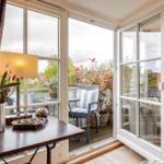 Terrasse mit Stuhl und Pflanzen. Blick ins Wohnzimmer mit Sofa und Wandbild.
