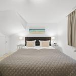 Bedroom with sloped ceiling, bed, nightstands, and window with curtains.