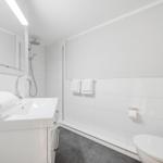 Bathroom with shower, sink, and toilet. White tiles and towels.