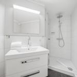 Bathroom with shower, sink, and mirror. White tiles and modern fixtures.