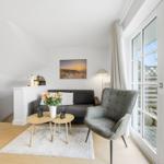 Living room with sofa, armchair, and table. Large window view to outdoor terrace.