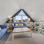 Wohn- und Essbereich mit blauen Sofas, Tisch und Stühlen unter Dachschrägen.