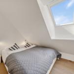 Schlafzimmer mit Dachfenster, Bett, Kissen und Holzboden.