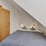 Schlafzimmer mit Dachschrägen, Bett mit Kissen und Holztür zu angrenzender Raum.