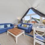 Zimmer mit zwei blauen Sofas, Tisch und Sitzgelegenheiten unter Dachschrägen.