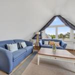 Wohnbereich mit blauen Sofas, Holztisch und großem Dachfenster mit Blick.