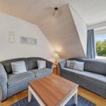 Zwei Sofas mit Kissen stehen um einen Holztisch herum. Fenster zeigt grüne Bäume. Holzdecke und Boden.