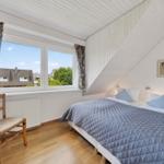 Schlafzimmer mit Dachschrägen, Bett, Stuhl und Fenster mit Blick.