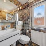 Badezimmer mit Waschbecken, Toilette und Fenster mit getöntem Glas.