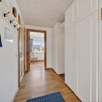 Flur mit weißen Schränken, Holzboden und Sicht auf Wohnzimmer.