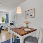 Essbereich mit Holztisch, Stühlen und Blumen. Wohnbereich mit Sofa und Fenster.